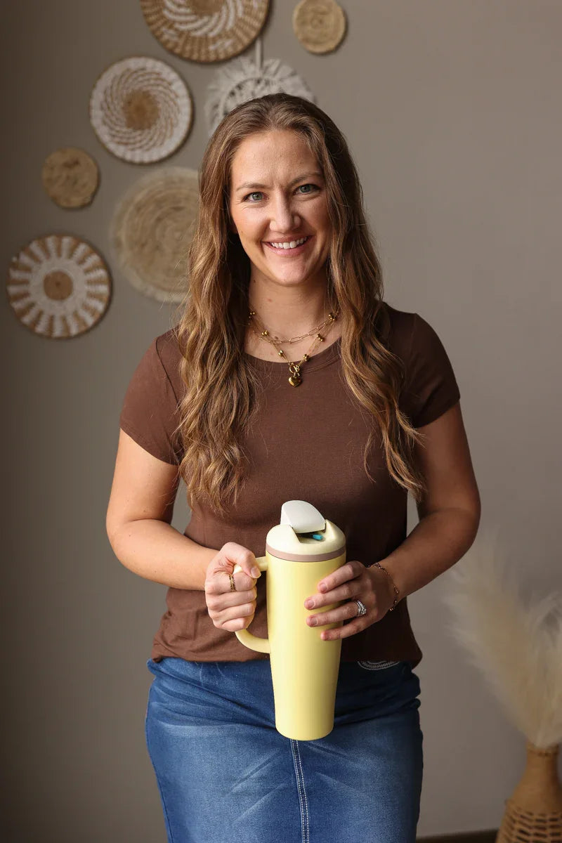 Woman holding a yellow mug in a room with decorative wall art.