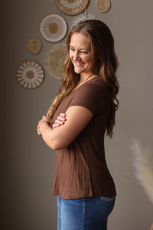 Woman wearing a brown shirt and blue jean skirt standing against a gray wall with decorative circular patterns.
