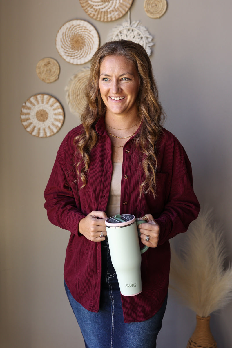 Front view of a wine corduroy button shirt layered open over a light top with a denim skirt.