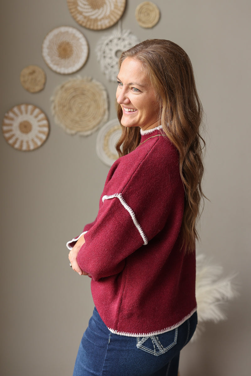 Side view of a cabernet mock neck sweater highlighting the light shoulder stitching and ribbed cuff.