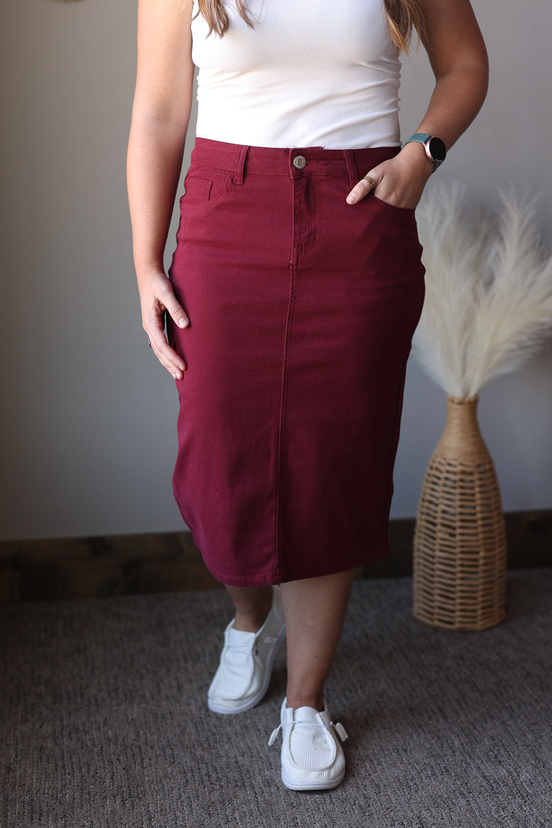 Person wearing a burgundy skirt and white sneakers in a room with a textured wall and decorative vase.