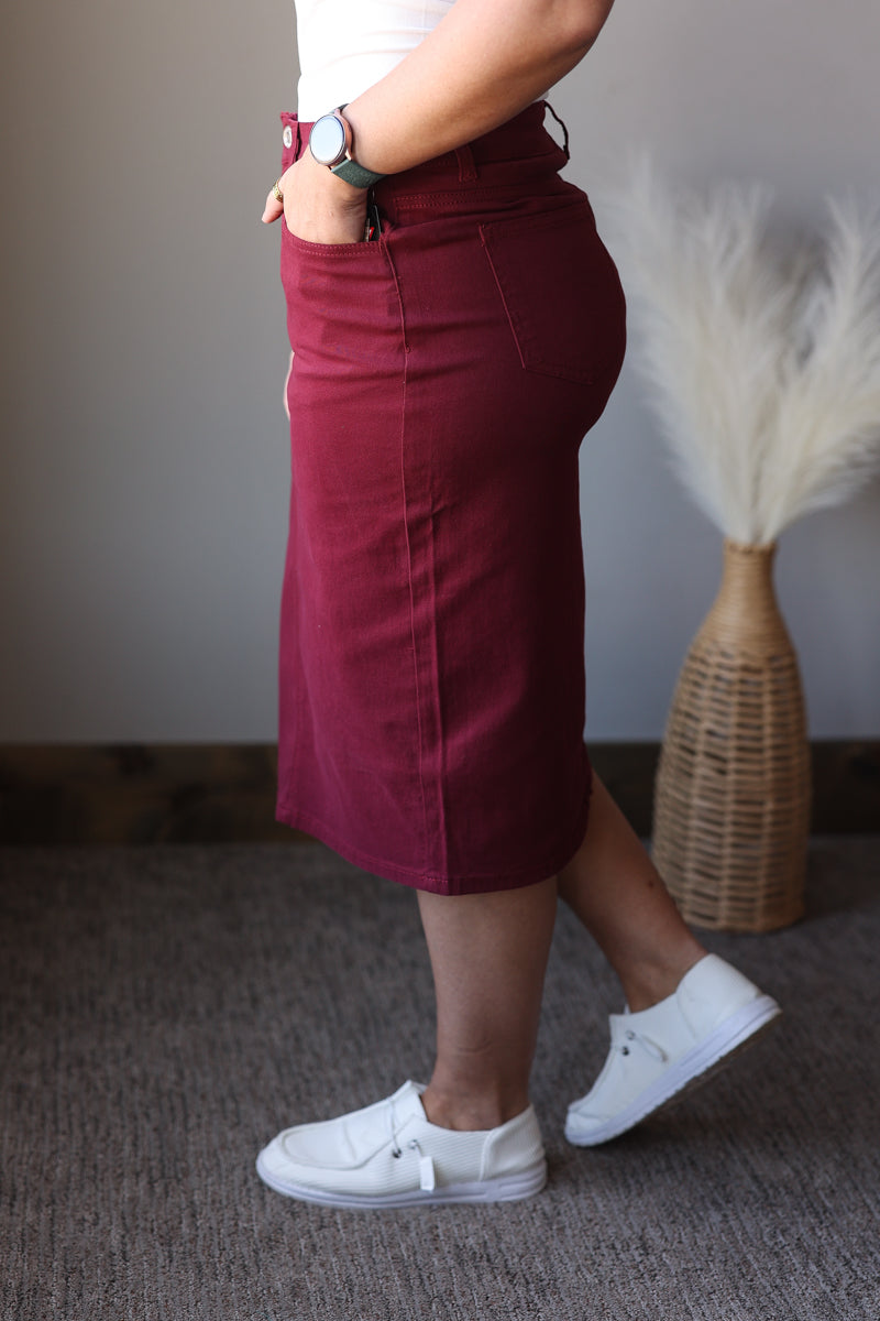 Person wearing a burgundy skirt and white sneakers in a room with a textured wall and decorative plant.