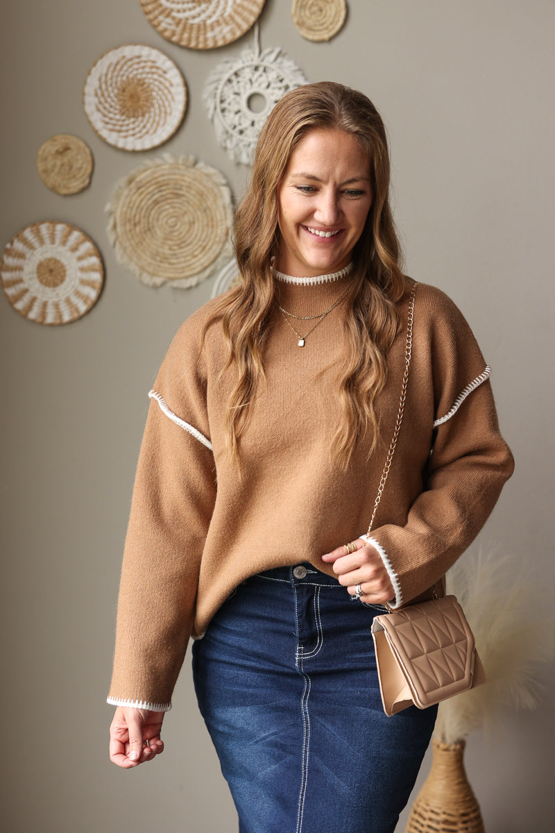 Front view of a camel mock neck sweater with a ribbed hem and light stitch details, worn with a denim skirt.
