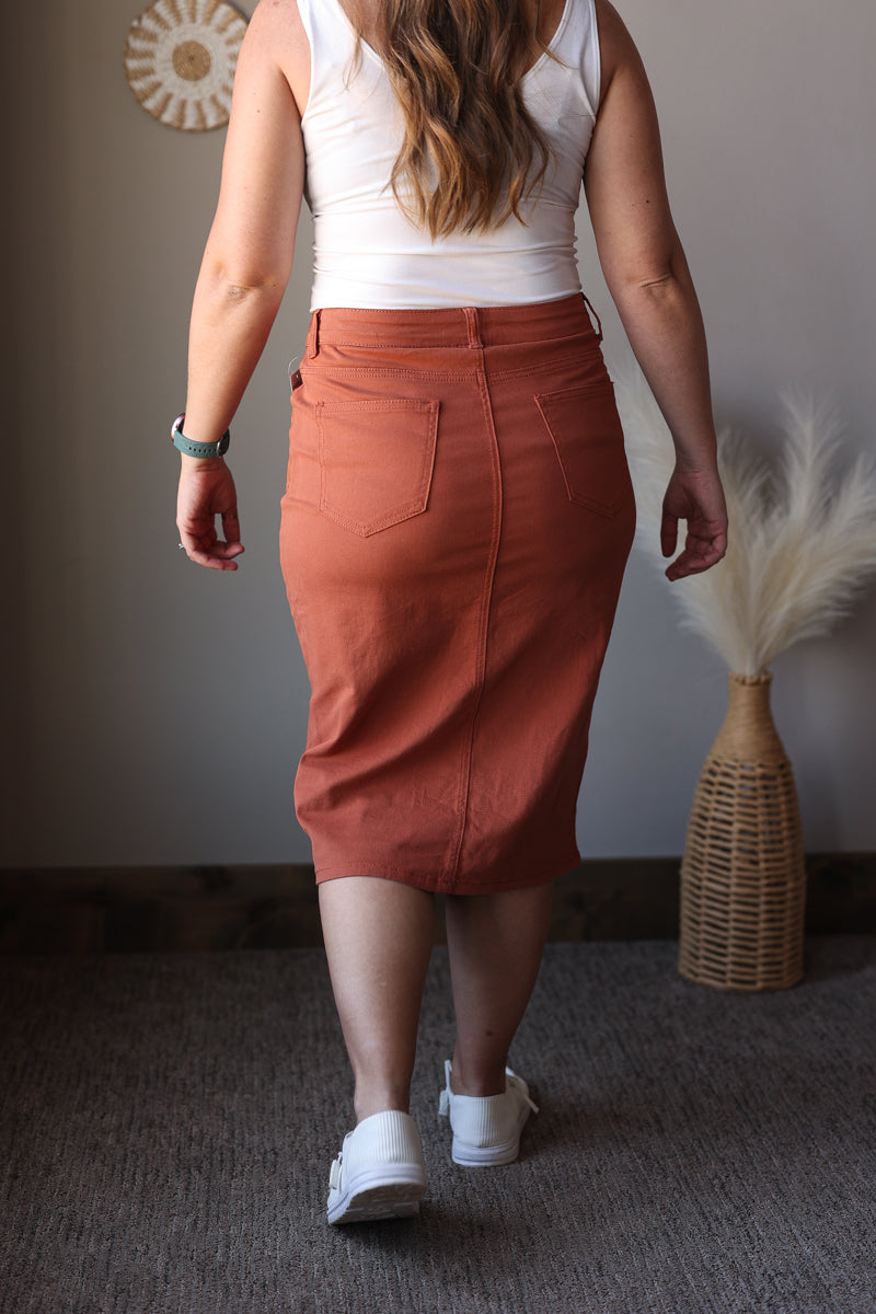 Person wearing a rust-colored skirt and white top indoors.