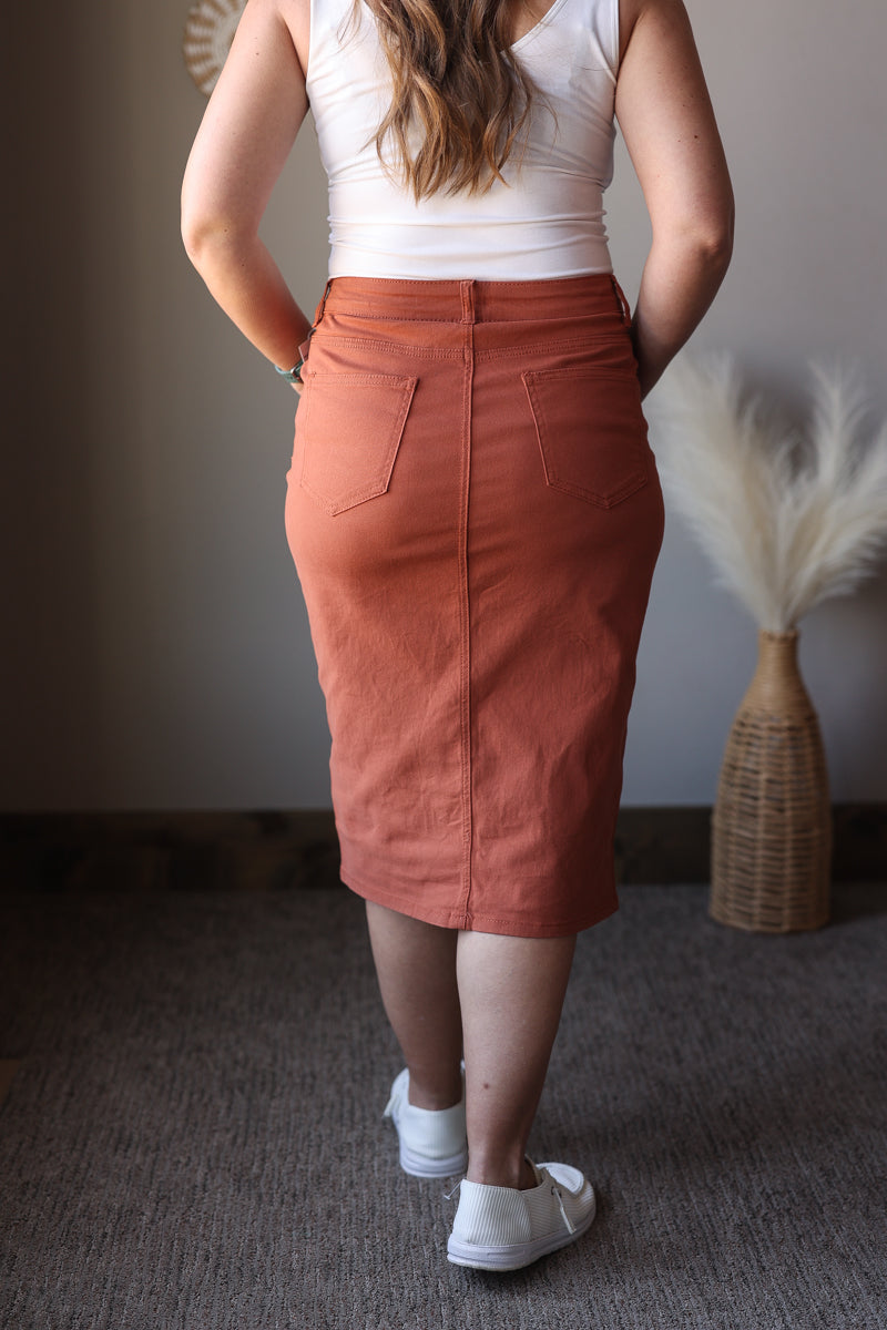 Person wearing a rust-colored skirt and white top indoors.