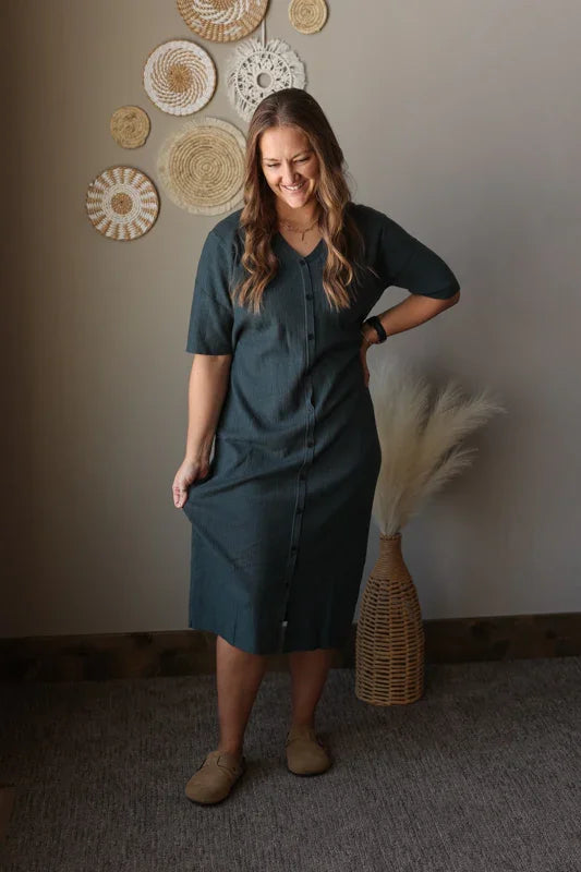 Woman in a gray dress standing in a room with decorative wall hangings.