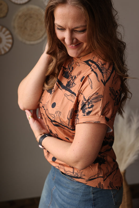 Woman wearing a patterned orange western t-shirt with black designs indoors.