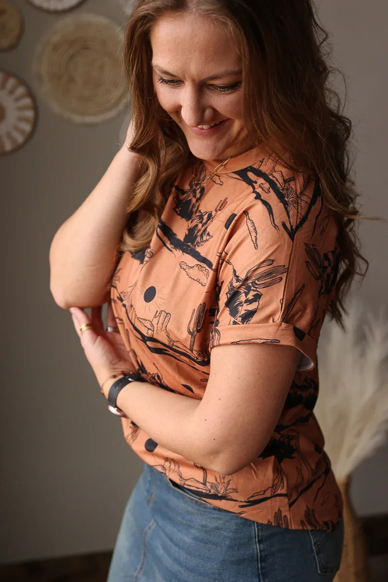Woman wearing a patterned orange western t-shirt with black designs indoors.