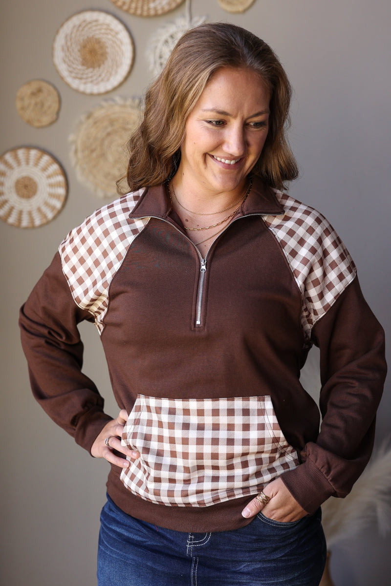 Brown quarter zip sweatshirt with hands in the plaid front pouch pocket, showing the collar and shoulder panels.