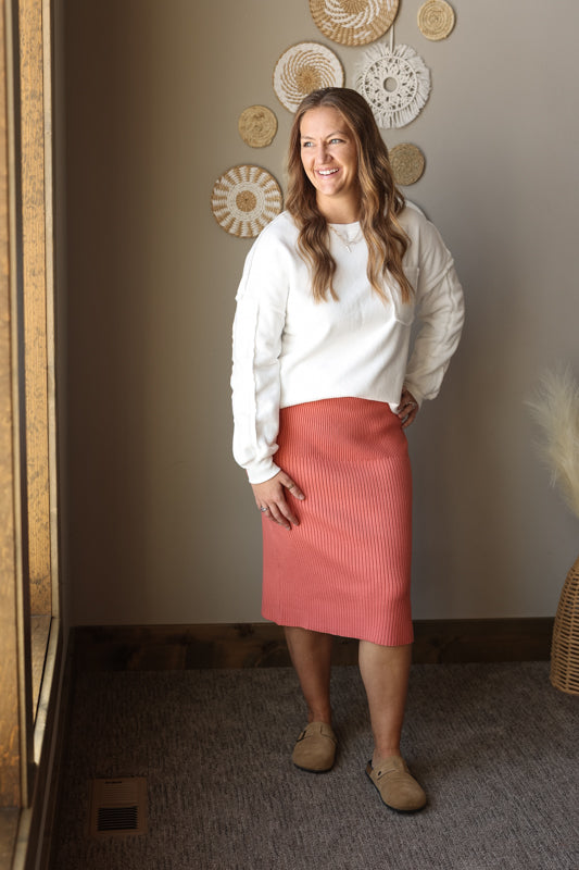 Woman wearing a white sweater and pink skirt standing in a room with decorative wall hangings.