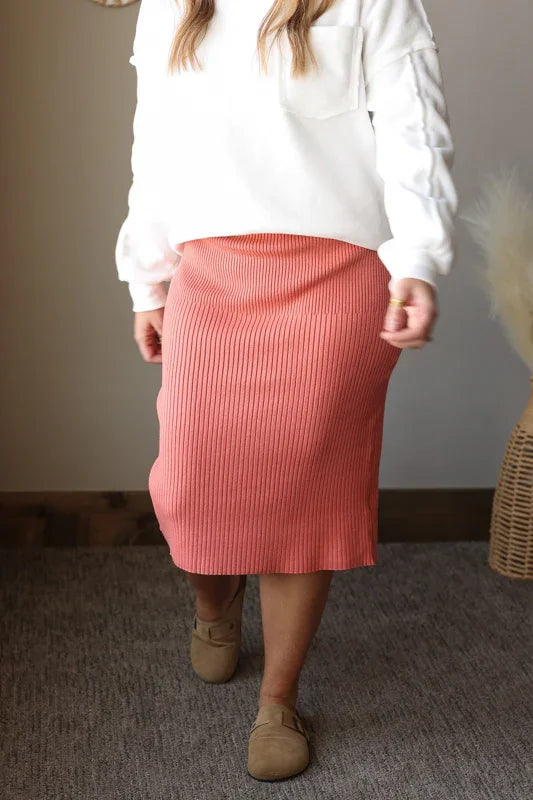 Person wearing a white sweater and pink skirt standing indoors.