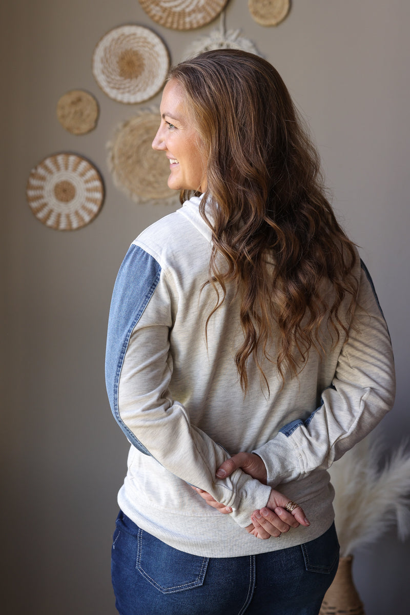 Back view of a light grey hoodie with a hood and contrasting blue denim sleeve panels.