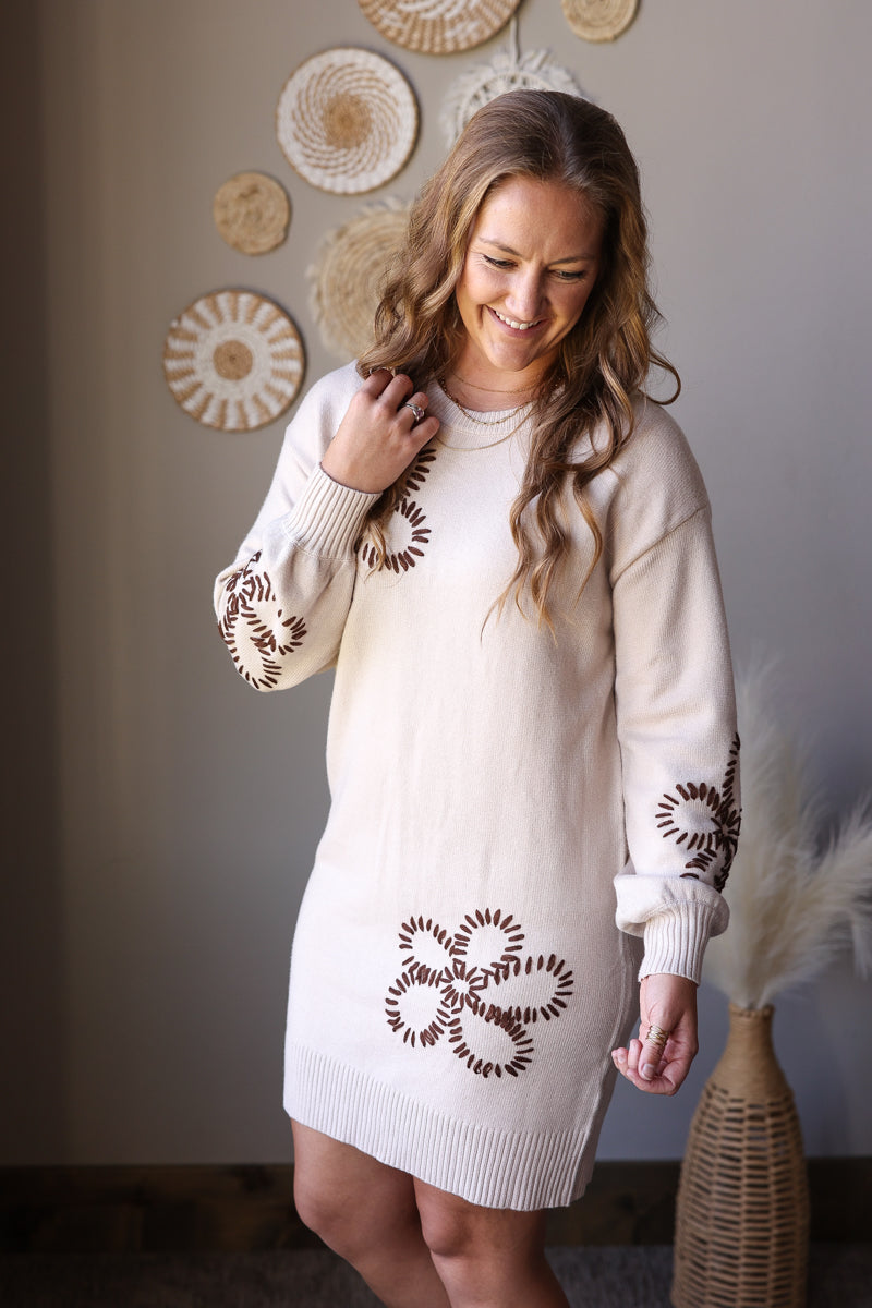 Close view of a parchment floral sweater dress highlighting its round neckline, puff sleeve, and flower details.