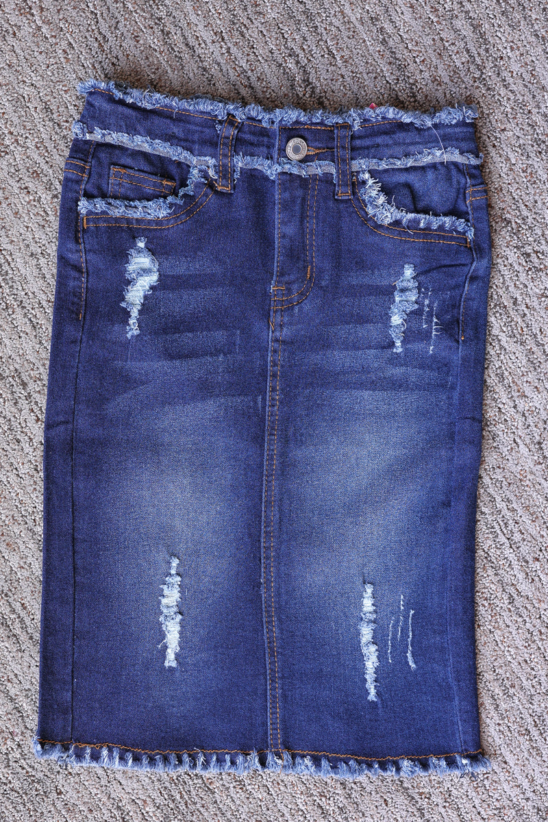 Front flat lay of a girls’ dark wash denim midi skirt with distressed details, front pockets, and a frayed hem.
