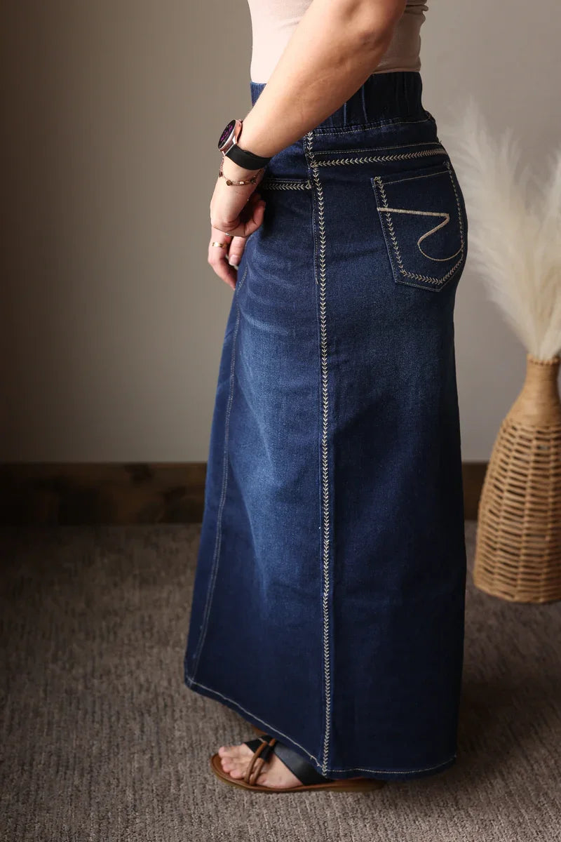 Person wearing a long blue denim skirt with a neutral background