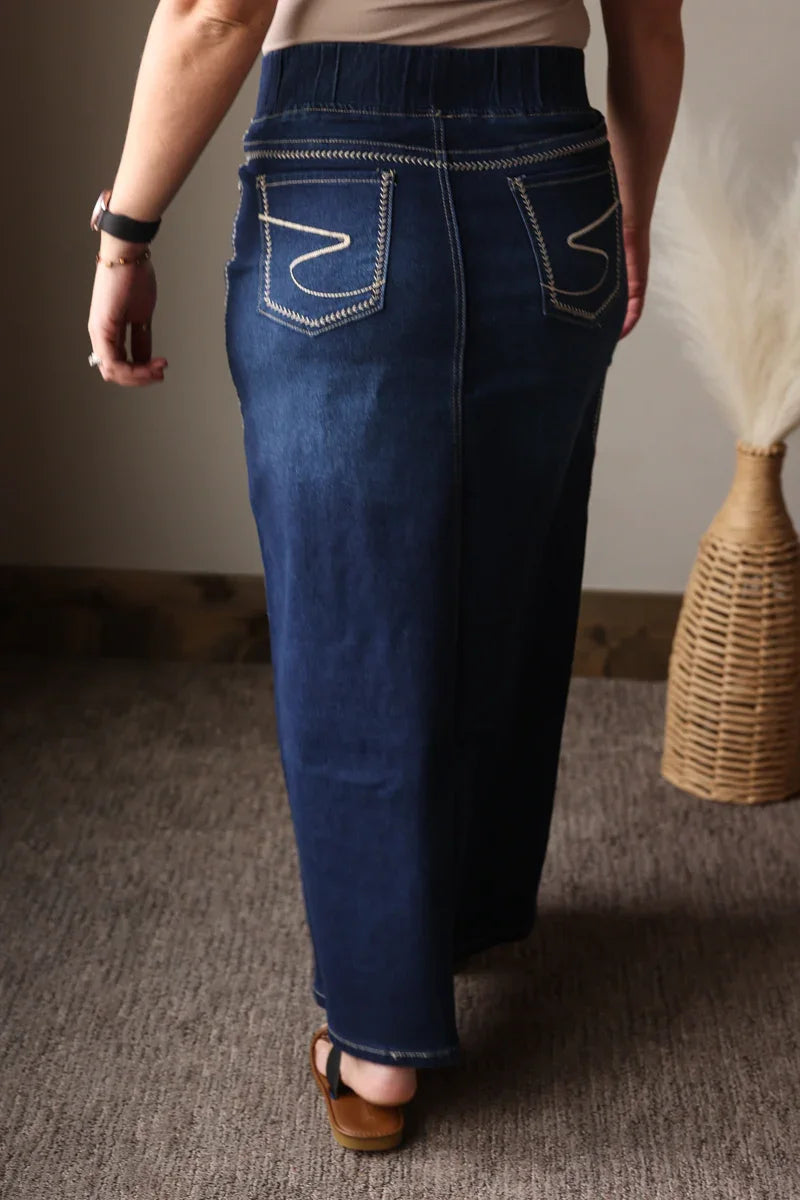 Person wearing blue jeans standing on a carpeted floor with a neutral wall and wicker basket in the background.