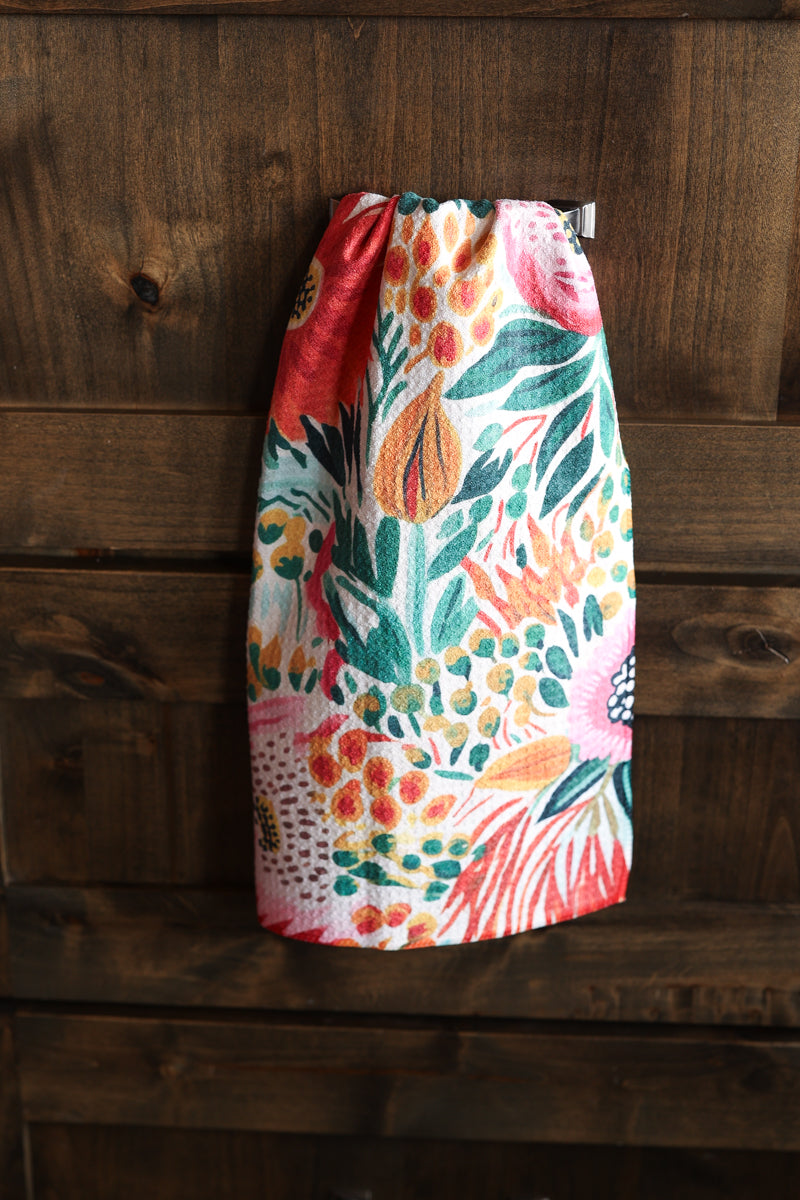 A colorful floral and botanical print skirt hanging against a dark rustic wooden plank wall.