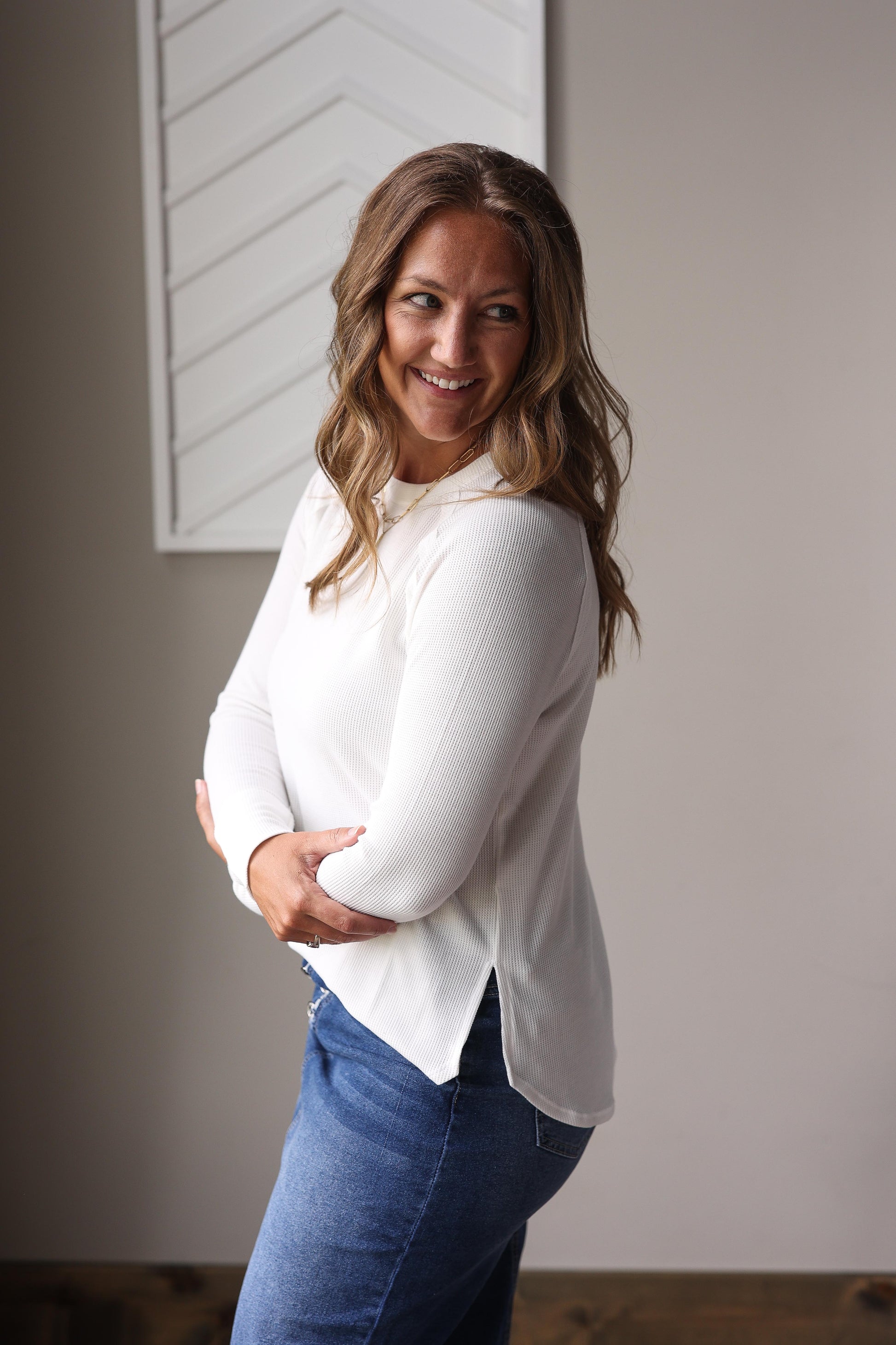 Woman wearing a white blouse and blue denim skirt standing against a neutral wall.