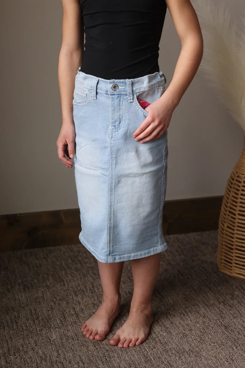 Person wearing a black top and light blue denim skirt standing on a carpeted floor.
