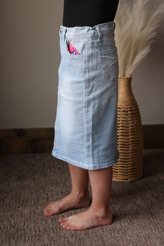 Person wearing a light blue denim skirt standing on a carpeted floor with a woven basket in the background.