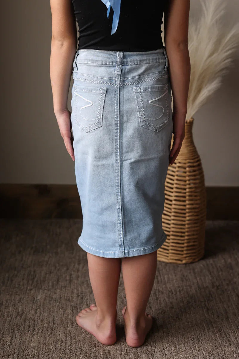 Person wearing a light blue denim skirt standing in a room with a woven basket.