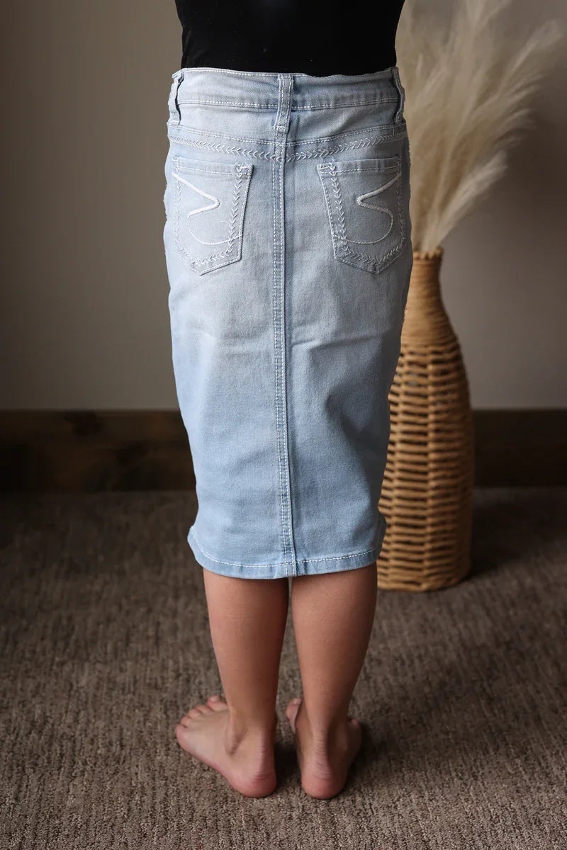Person wearing a light blue denim skirt standing on a carpeted floor with a woven basket in the background.
