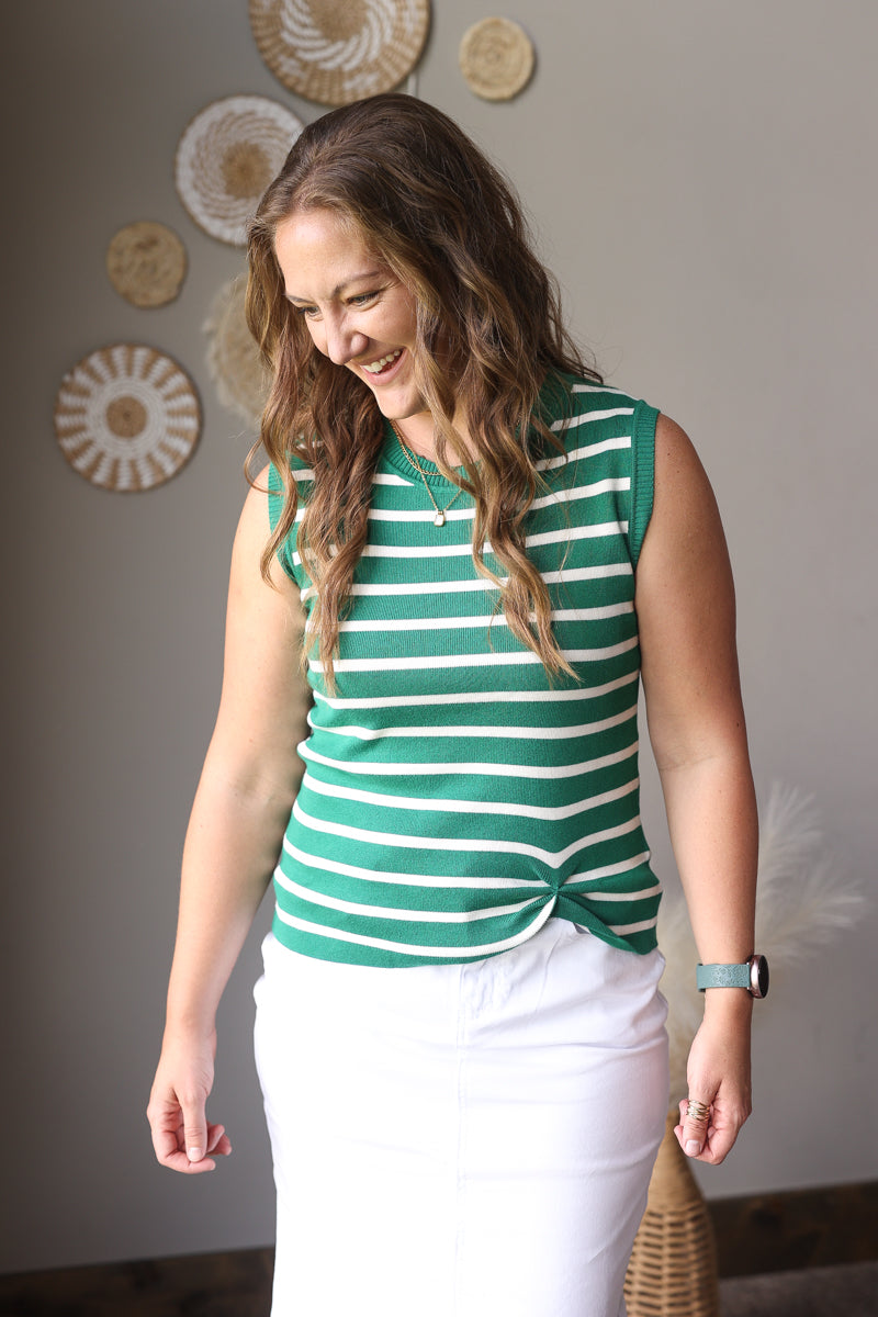 Woman wearing a green and white striped shirt and white skirt standing indoors.