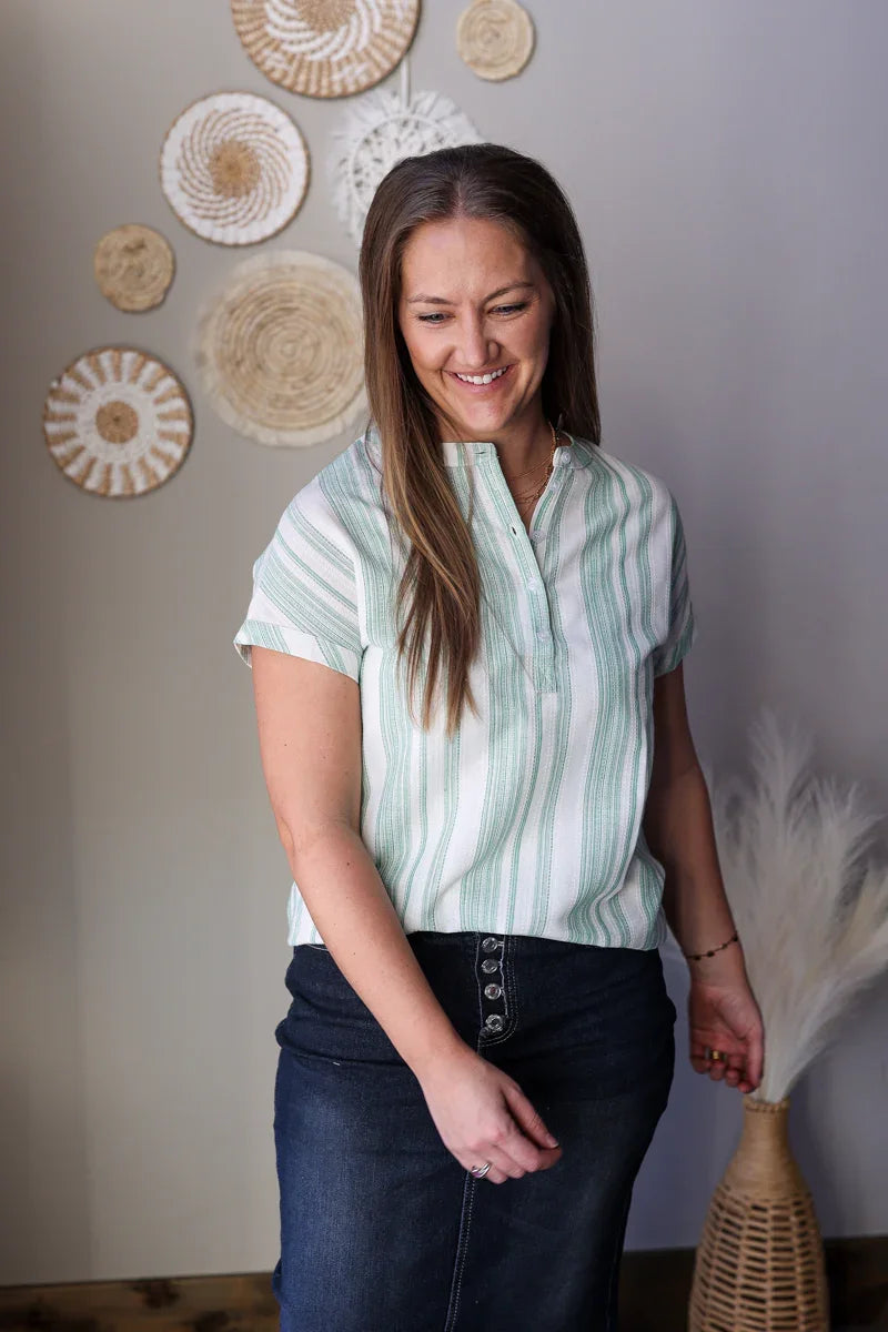 Woman wearing a light green blouse with short sleeves, standing in a room with decorative wall art.