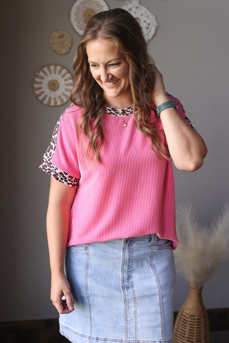 Woman wearing a pink top with leopard print sleeves in a room setting.