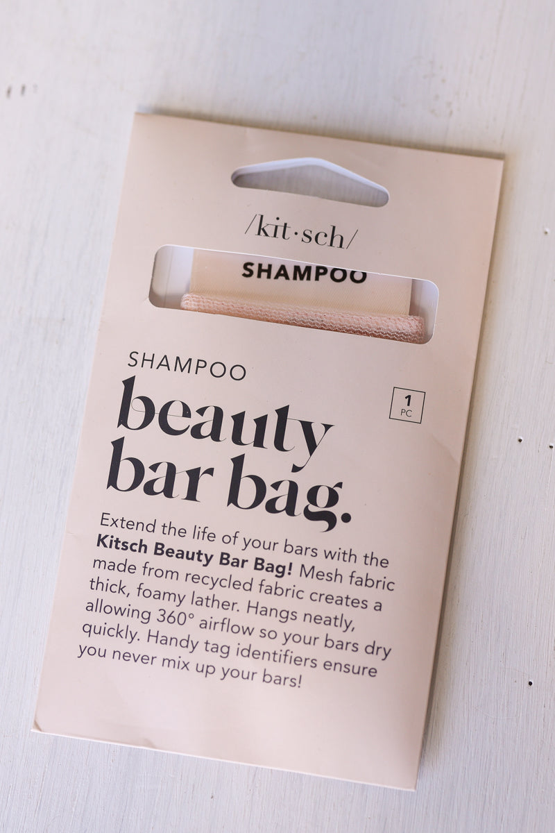 Kitsch Beauty Bar Bag Shampoo packaging card with a single beige shampoo bar visible through a cutout window, photographed on a light wood surface.