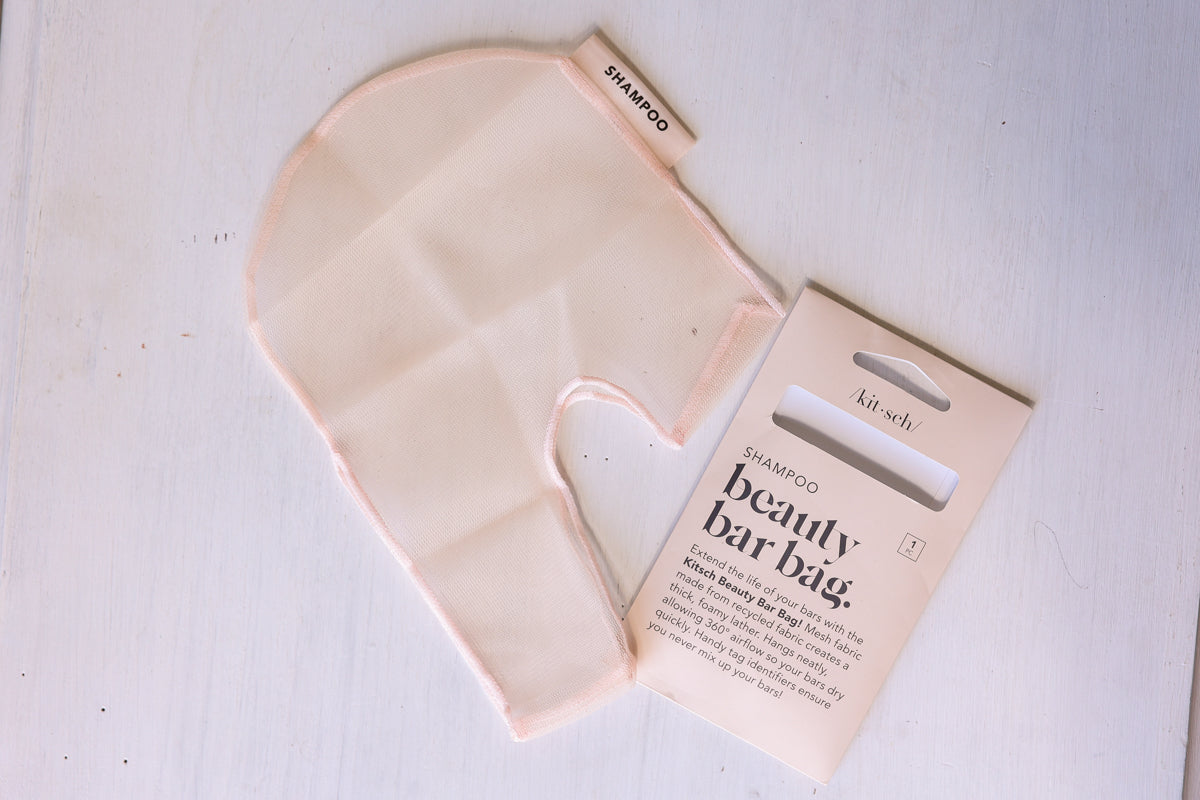A pale blush pink silicone beauty bar bag with its matching kraft paper packaging card, displayed on a white wooden background.