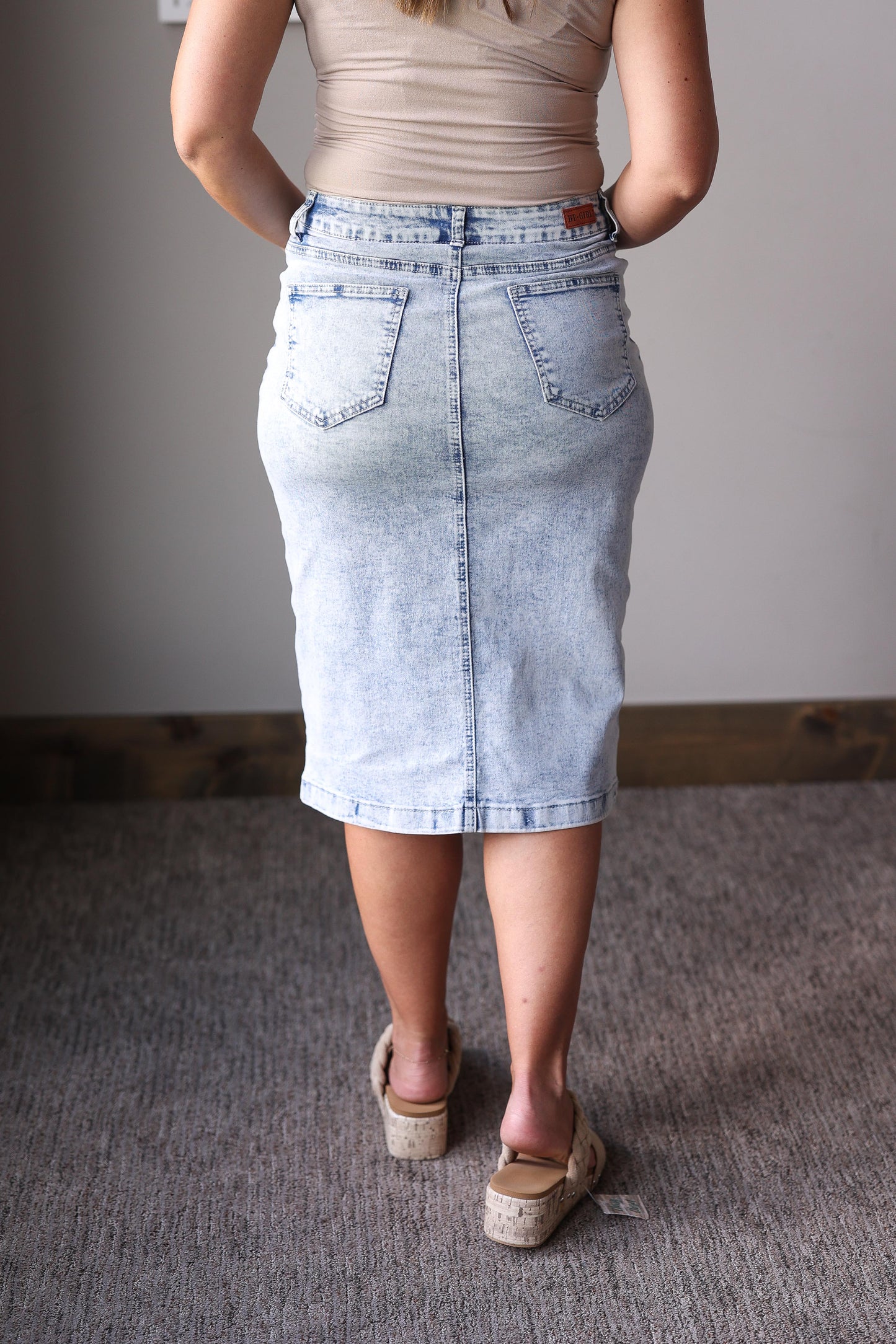 Person wearing a light blue denim skirt and beige sandals on a neutral background