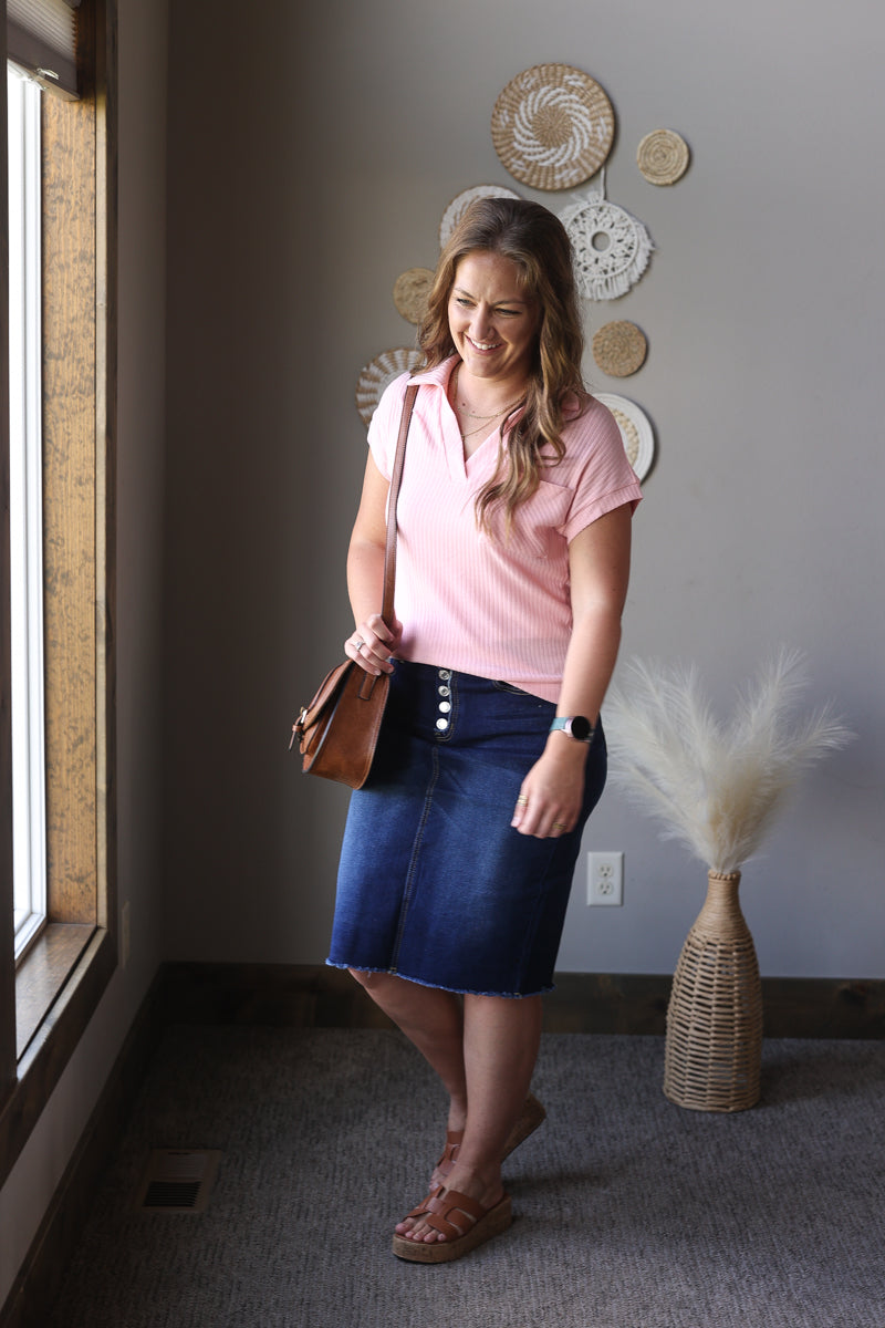 Woman in pink shirt and blue skirt standing in a room with decorative wall art.