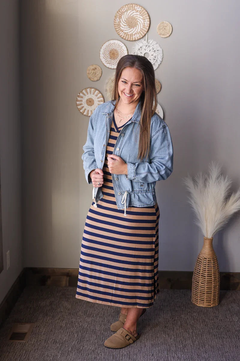 Woman wearing a denim jacket over a striped dress in a room with decorative wall art and a vase.