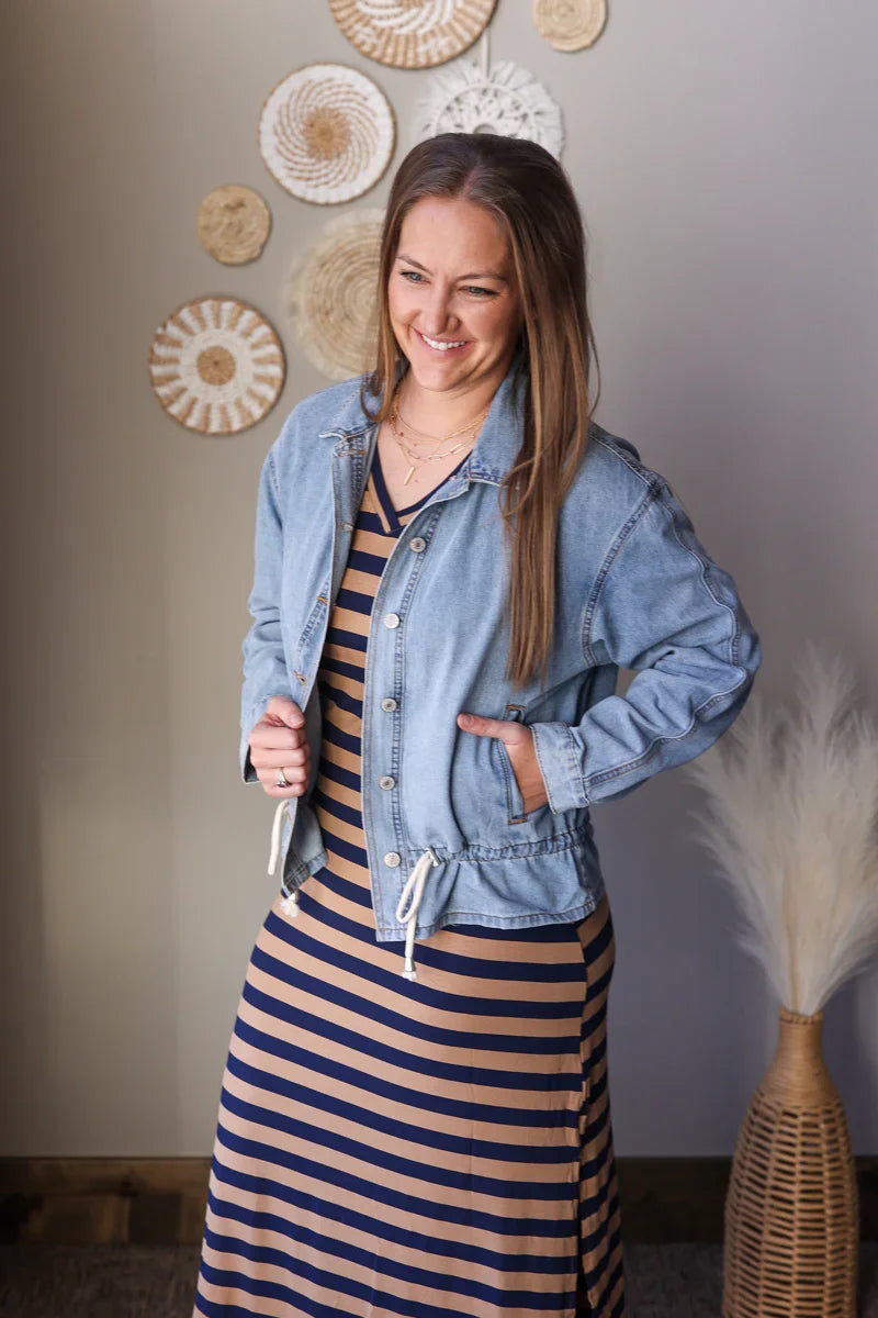 Woman wearing a denim jacket over a striped dress in a room with decorative wall art.