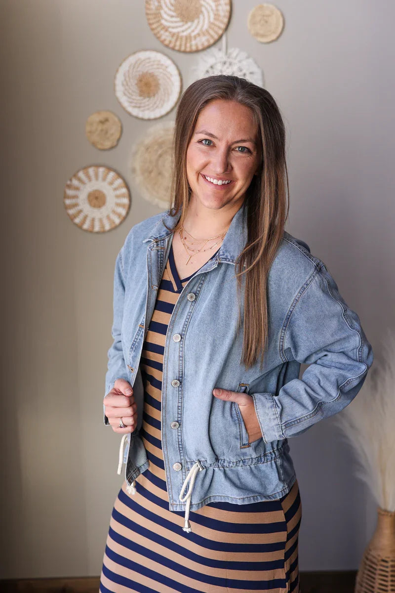 Woman wearing a striped dress and denim jacket indoors with decorative wall items.