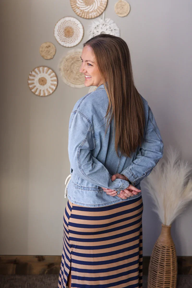 Woman wearing a denim jacket and striped skirt standing in front of decorative wall art.