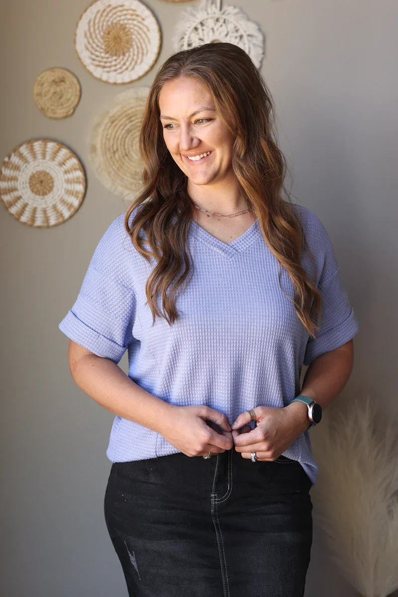 Woman wearing a light purple shirt and black skirt standing against a wall with decorative circular objects.