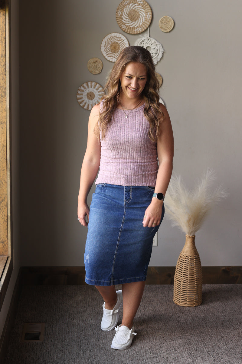 Woman wearing a pink top and blue skirt standing in a room with decorative wall art.