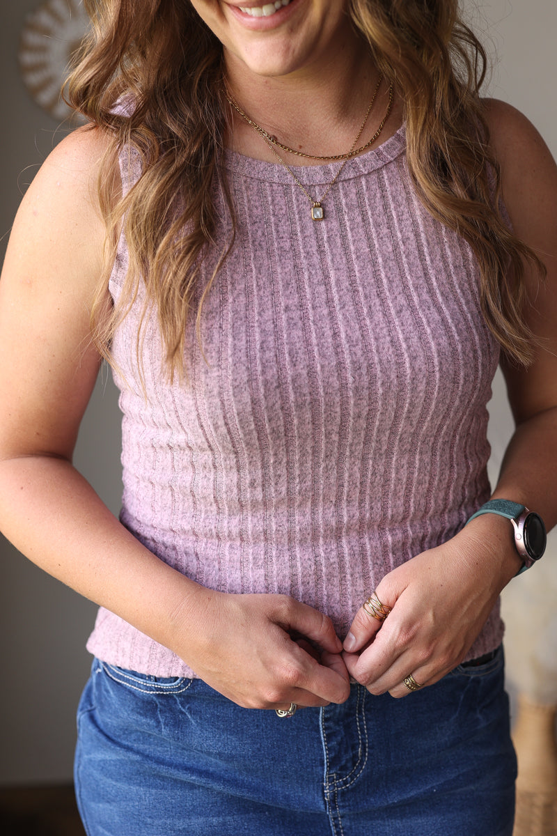 Woman wearing a purple sleeveless top and blue jean skirt, smiling.