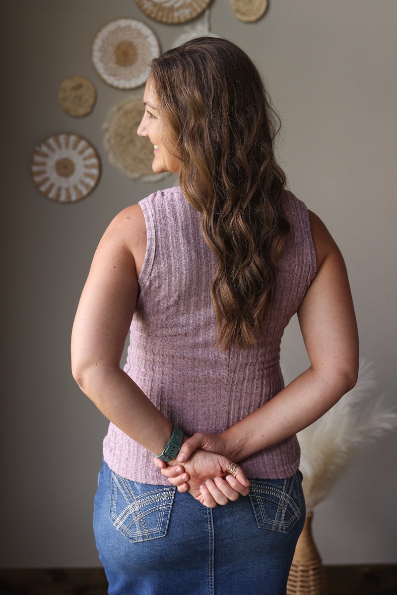 Woman wearing a pink sleeveless top and blue jean skirt standing in a room with decorative wall art.
