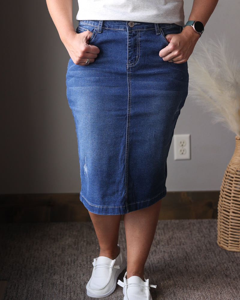 Person wearing a blue denim skirt and white sneakers indoors.