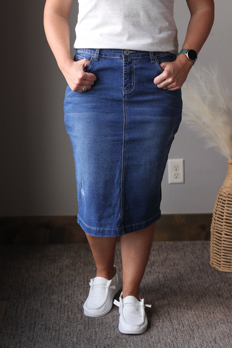 Person wearing a blue denim skirt and white sneakers indoors.
