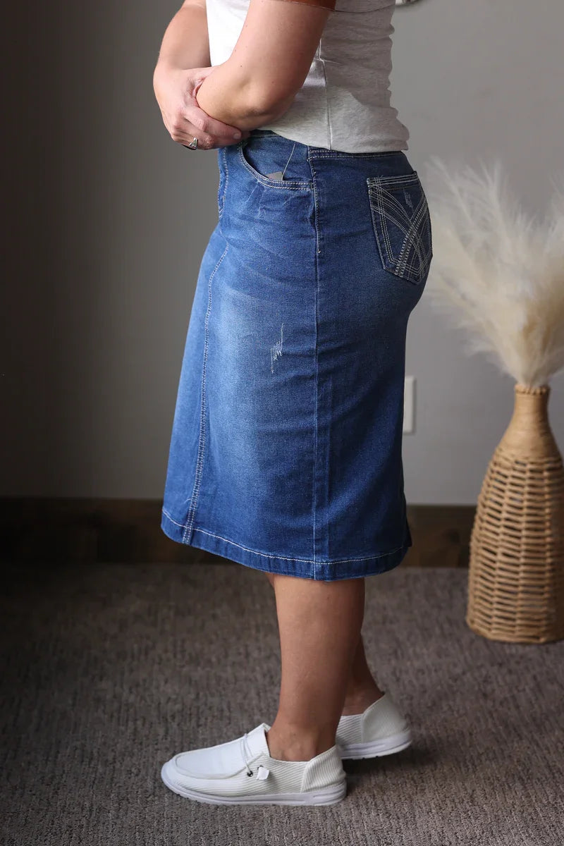 Person wearing a blue denim skirt with a plain background