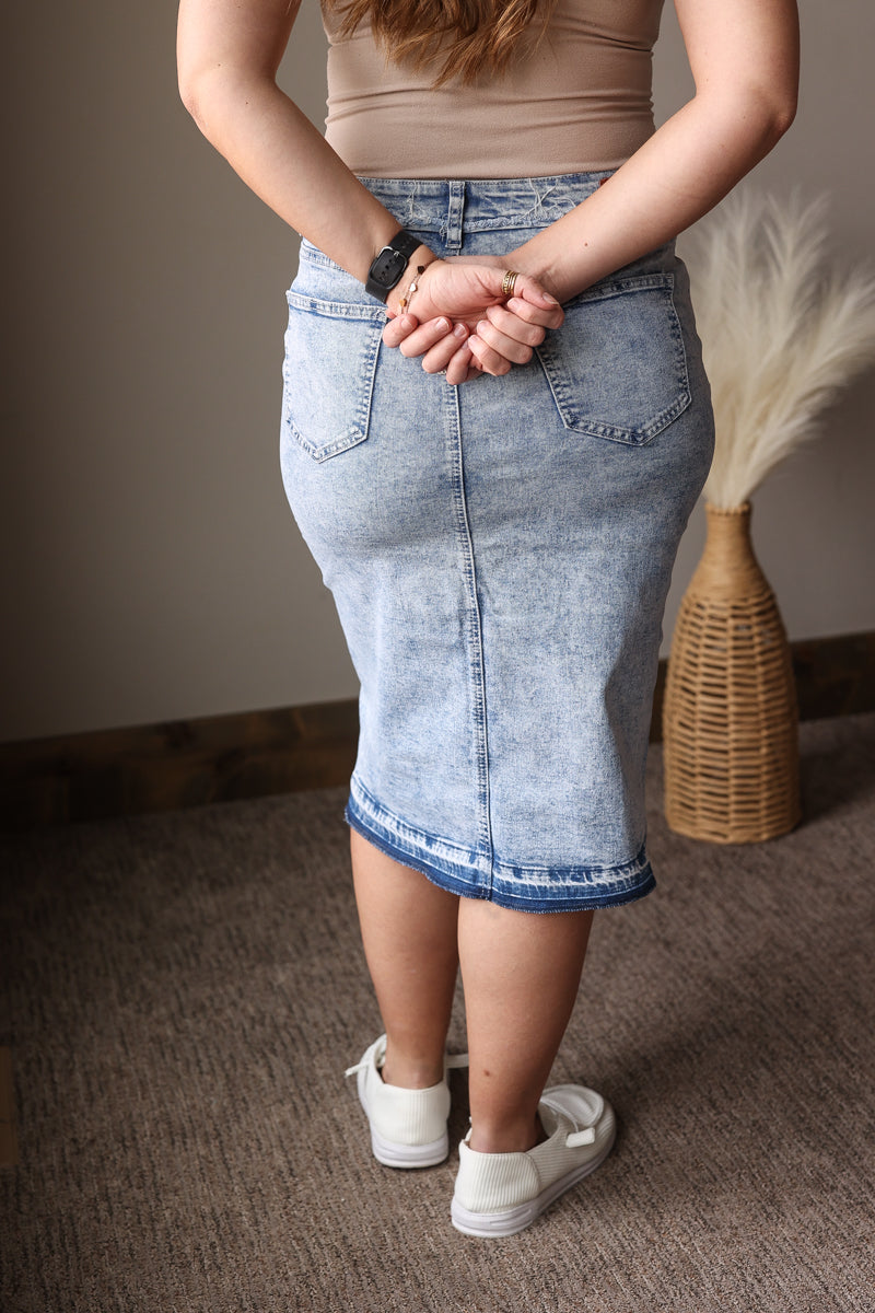 Person wearing a denim skirt standing on a carpeted floor with a neutral wall in the background.