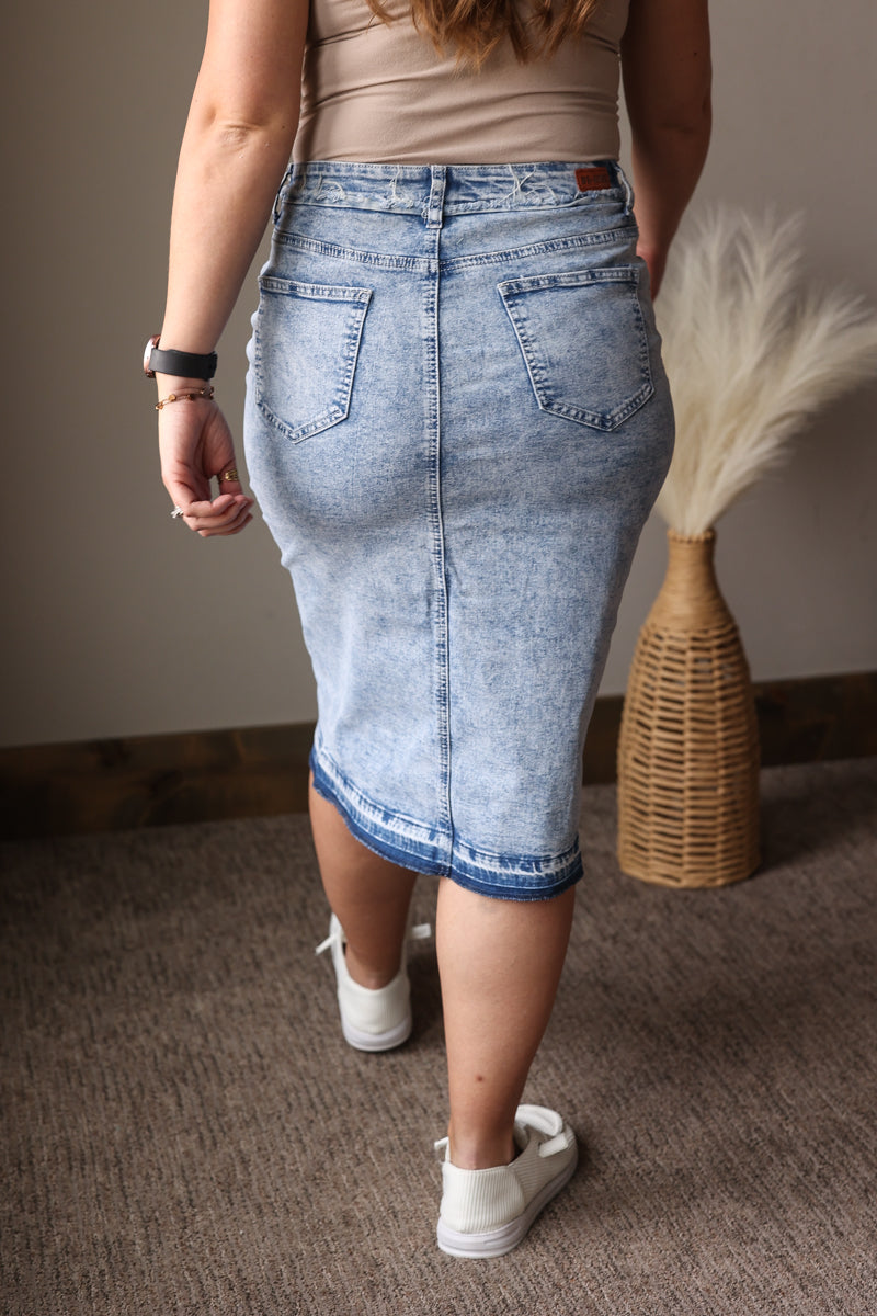 Person wearing a light blue denim skirt with a neutral background