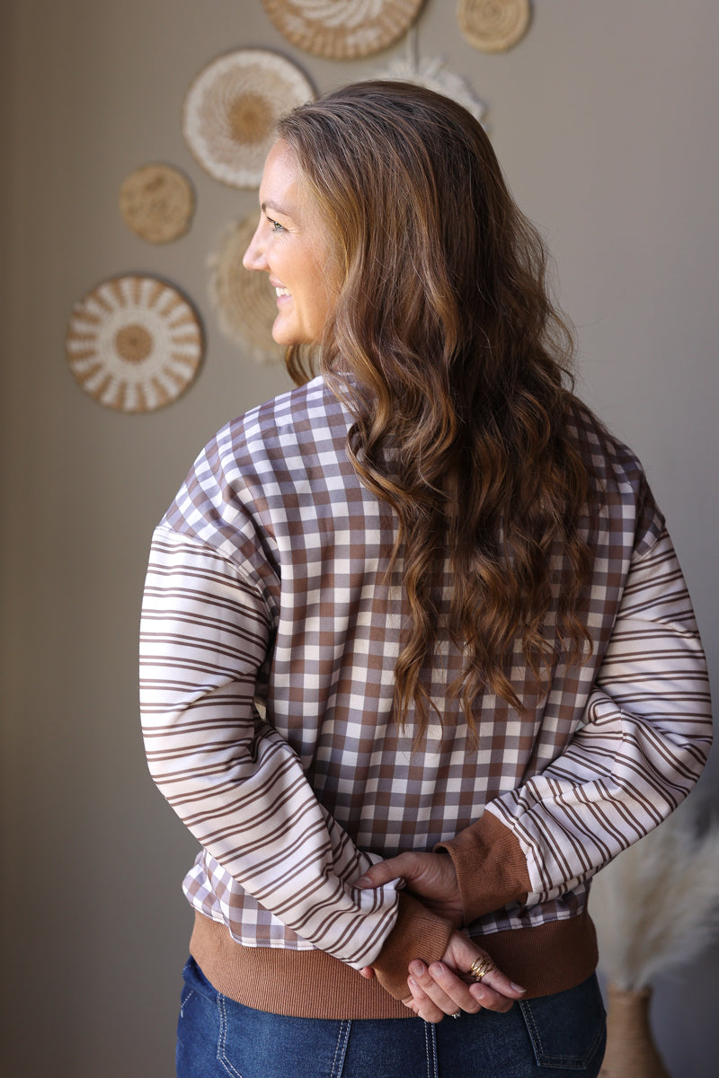 Angled back view of a brown and cream plaid top with contrasting striped long sleeves.
