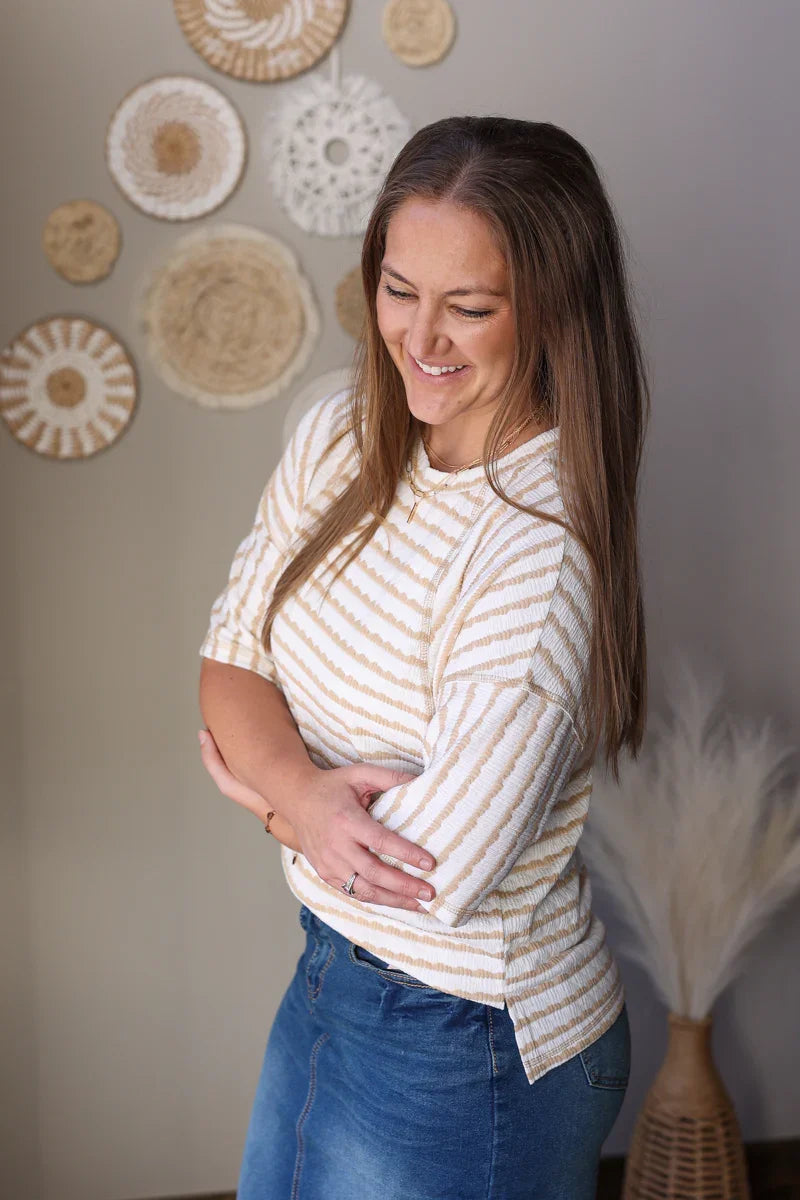 Woman wearing a striped shirt and jean skirt standing in front of decorative wall art.