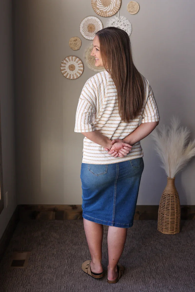 Woman wearing a striped shirt and blue skirt standing in a room with decorative wall art.