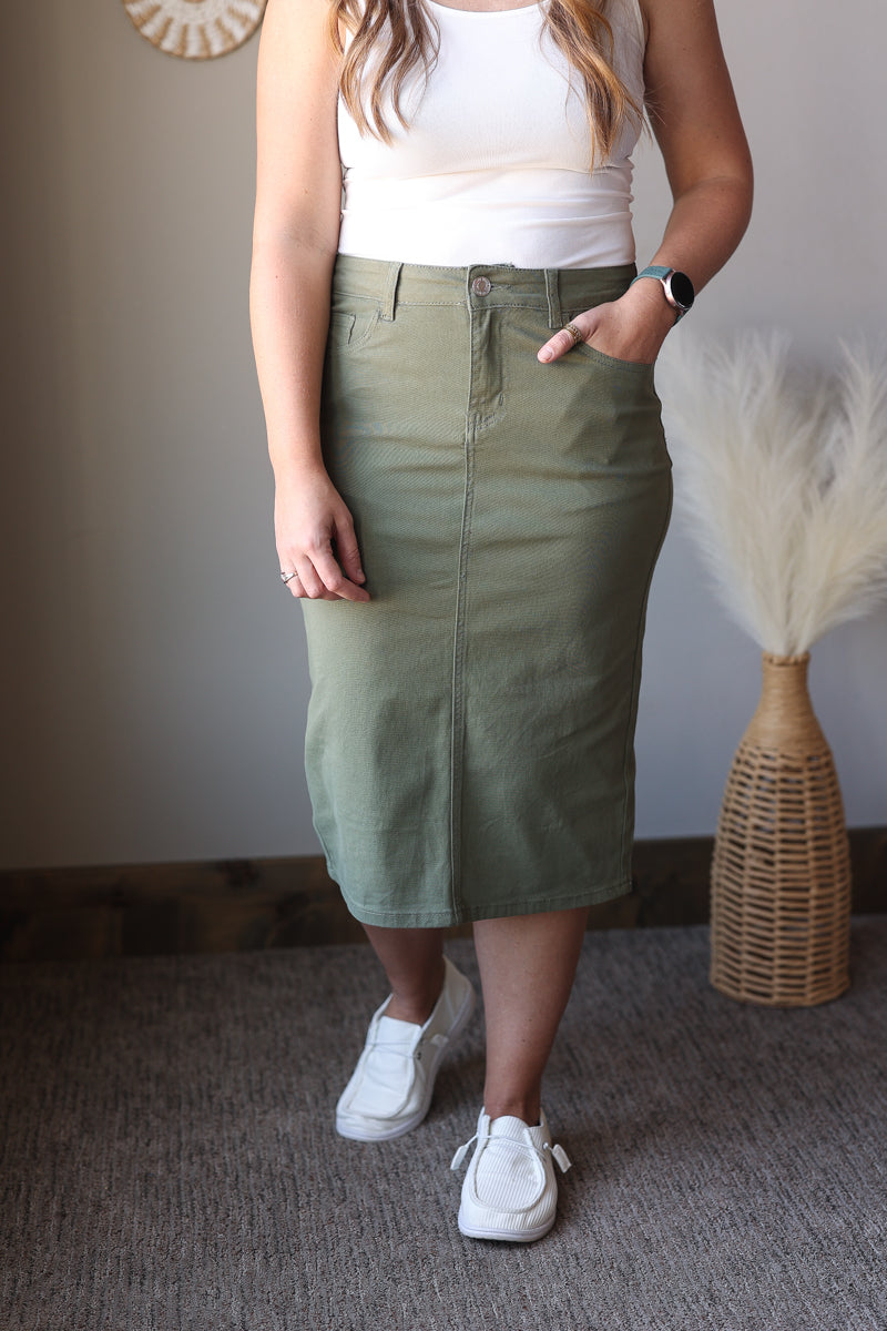 Person wearing a white tank top and green skirt with white sneakers indoors.